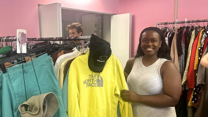 A young woman smiles while holding a yellow hoodie in a clothing store while a young man browses off to the side.