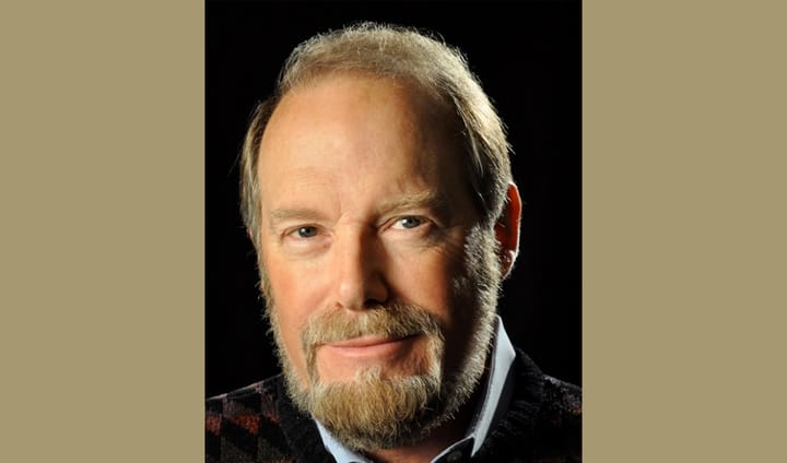 A man with a sandy beard and nice smile looks intently at the camera.