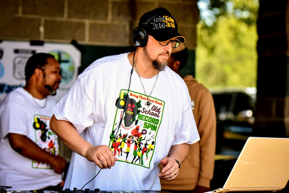 Tall man works at a music console, playing hip-hop music. 