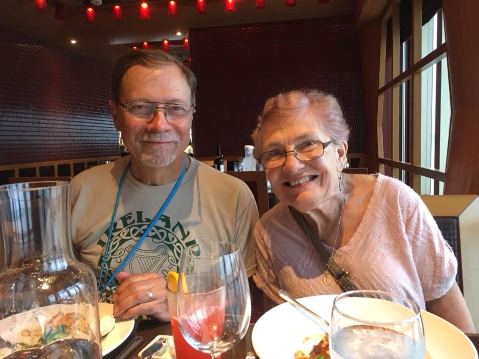 A man and his wife sit at a dinner table in a restaurant smiling at the camera.